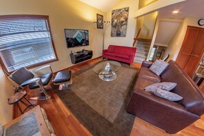 A living room with a red sofa, a glass coffee table, and a TV on the wall.