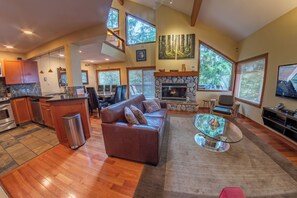 A spacious living area with a stone fireplace, a leather sofa, and a glass coffee table. - Snowy Creek 4 - Ski in Ski out, Private Hot Tub, Short Walk to Whistler Village (Whistler)