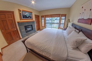 Un dormitorio con una cama grande, chimenea, balcón con vistas y una puerta.