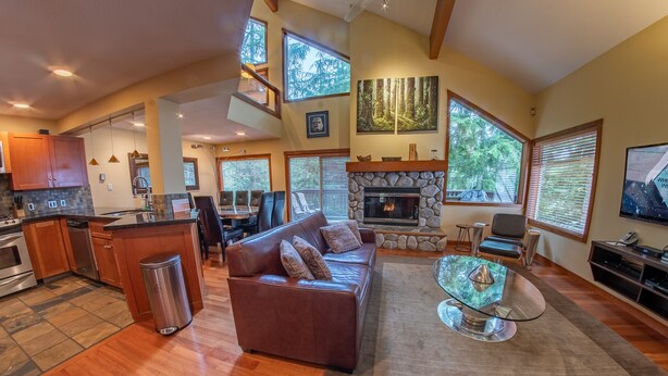 A spacious living area with a stone fireplace, a leather sofa, and a glass coffee table. - Snowy Creek 4 - Ski in Ski out, Private Hot Tub, Short Walk to Whistler Village (Whistler)