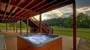 Un jacuzzi bajo una pérgola de madera, con vistas a un campo cubierto de césped y árboles.