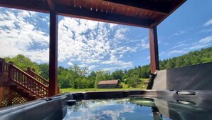A hot tub under a wooden pergola with a view of a house and trees.