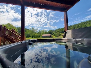 A hot tub under a wooden pergola with a view of a house and trees.