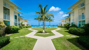 Un resort con un camino central que lleva a una palmera, rodeado de céspedes cuidados y vistas al océano.