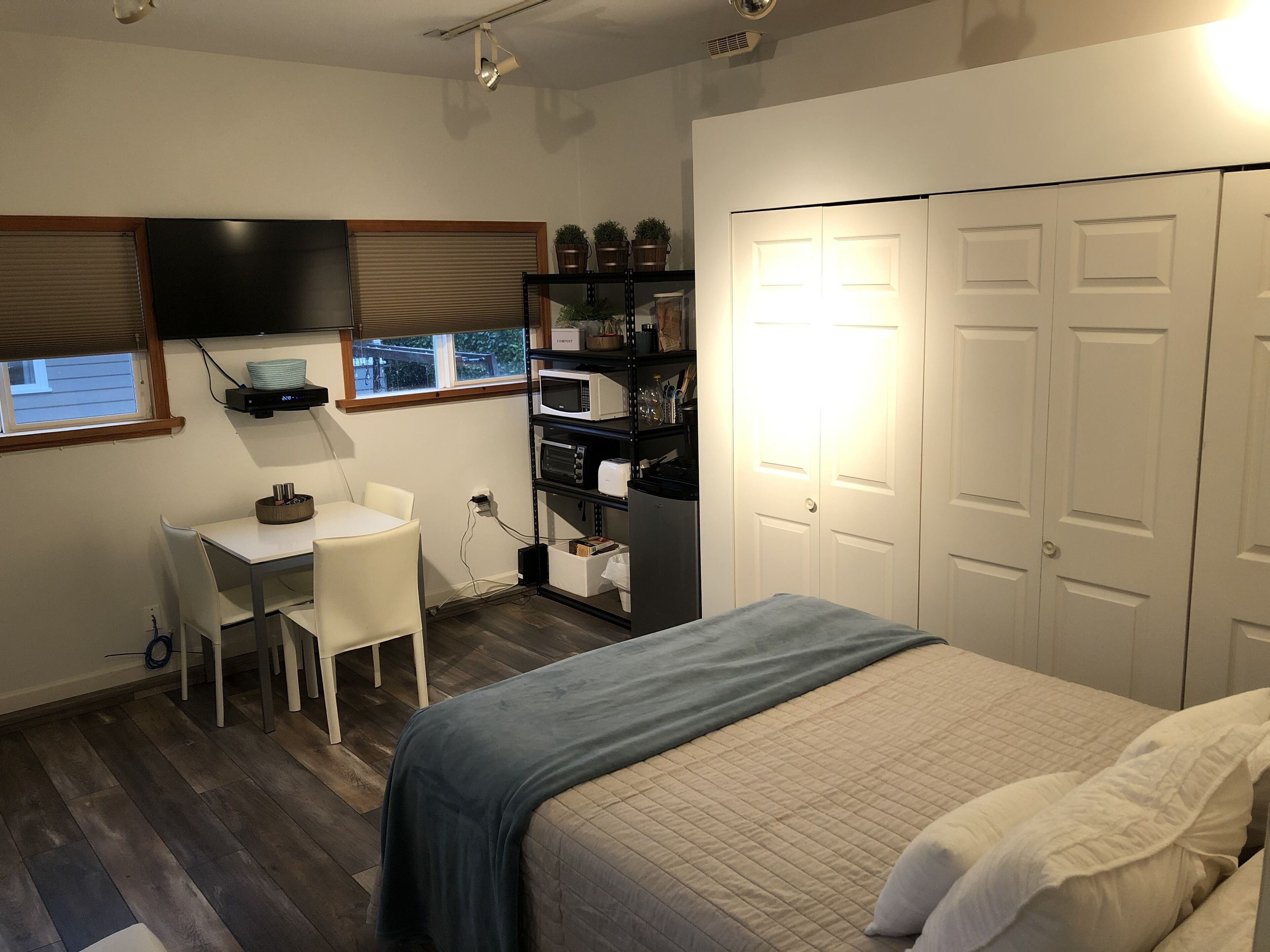 A compact bedroom with a bed, a desk, and a TV mounted on the wall.