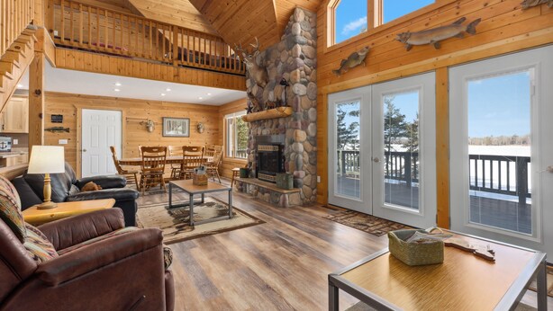 A spacious living room with a stone fireplace, wooden ceiling, and large windows.