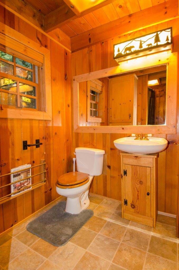 A wooden cabin bathroom with a toilet, sink, and mirror.