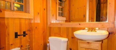 A wooden cabin bathroom with a toilet, sink, and mirror.