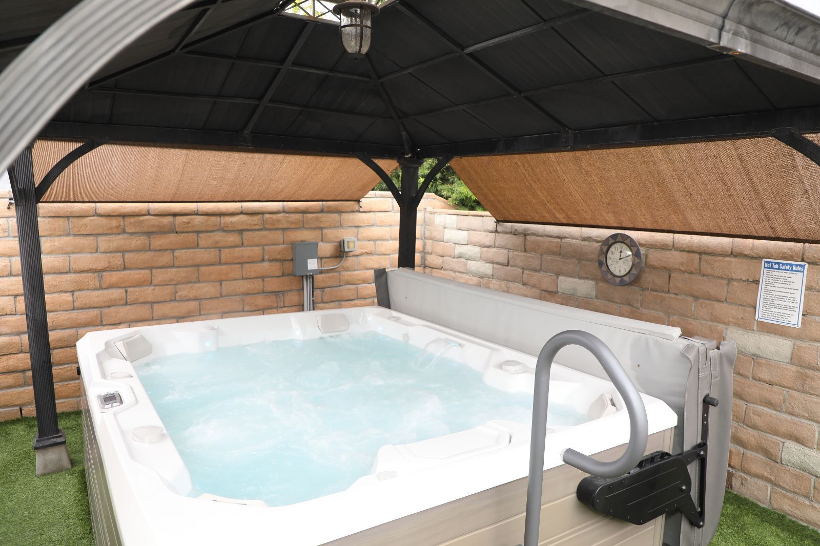 An outdoor hot tub under a covered area with a brick wall and a safety sign.