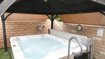 An outdoor hot tub under a covered area with a brick wall and a safety sign.