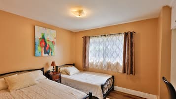 A bedroom with two beds, a nightstand, a lamp, a painting, and a window with curtains.