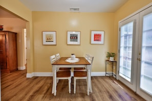 Ein Essbereich mit Holztisch und Stühlen, Bildern an der Wand und einer Tür mit Jalousien.