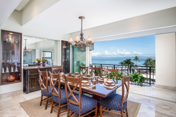 Uma área de jantar com uma mesa grande, cadeiras e vista para o oceano.