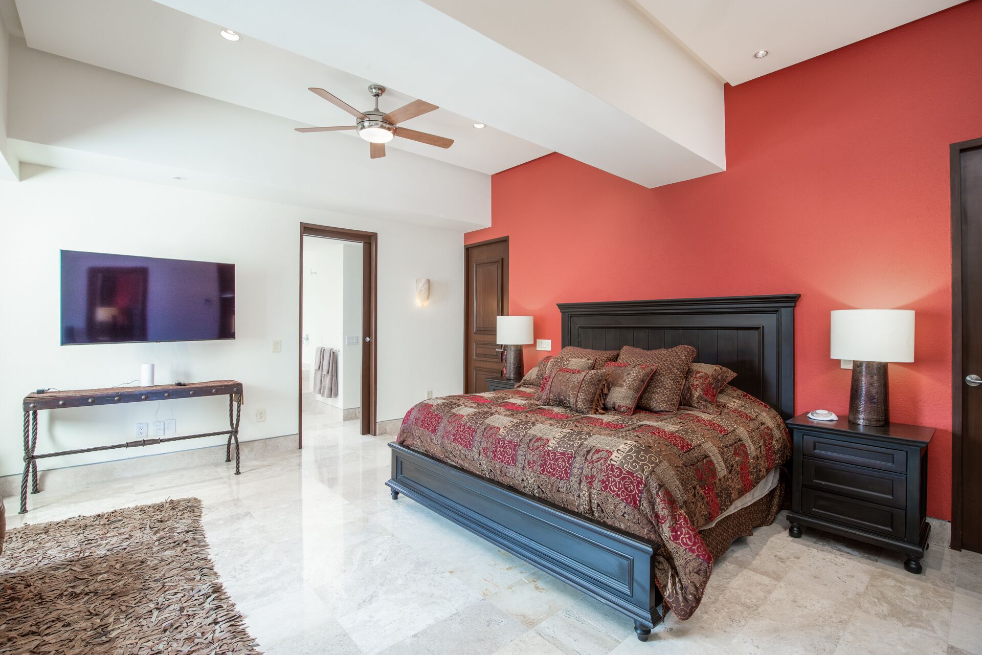 A bedroom with a bed, nightstands, a TV, and a ceiling fan.