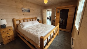Une chambre à coucher aux murs lambrissés, avec un lit, des tables de chevet et une porte donnant sur une autre pièce.