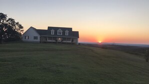 Et stort hus med en rummelig græsplæne og solnedgang i baggrunden.