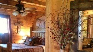 Et hyggeligt træhusværelse med seng, et skrivebord med en bærbar computer, en vase med blomster og en loftsvifte.