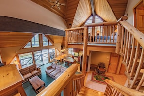 A spacious loft-style room with a high ceiling, wooden beams, and a mezzanine level with a balcony.