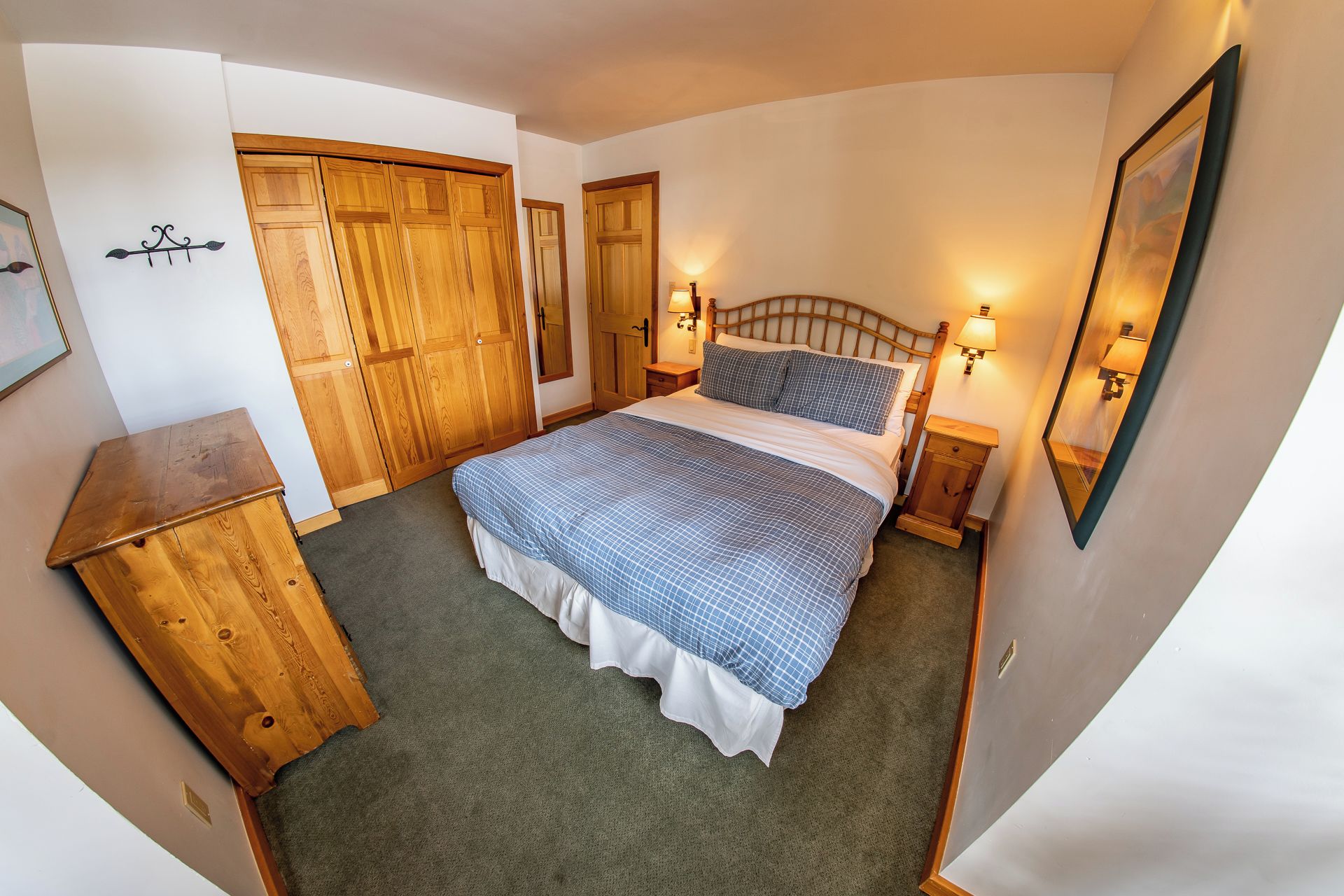 Un dormitorio con cama, armario de madera, mesitas de noche y lámparas de pared.