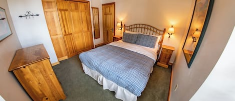 Un dormitorio con cama, armario de madera, mesitas de noche y lámparas de pared.