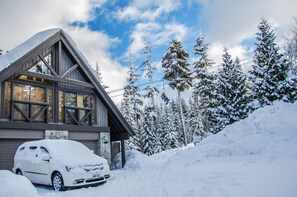 A cabin with a sloped roof, large windows, and a car parked in front.