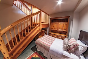 A bedroom with a wooden staircase, a bed with a plaid bedspread, a wardrobe, and a small desk.