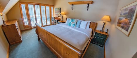 A bedroom with a large bed, wooden headboard, two bedside tables with lamps, a wooden dresser, and a window with blinds.