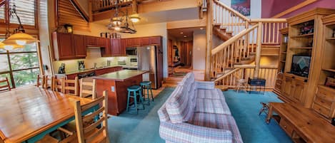 A spacious living area with a wooden staircase, a dining table with chairs, and a sofa.