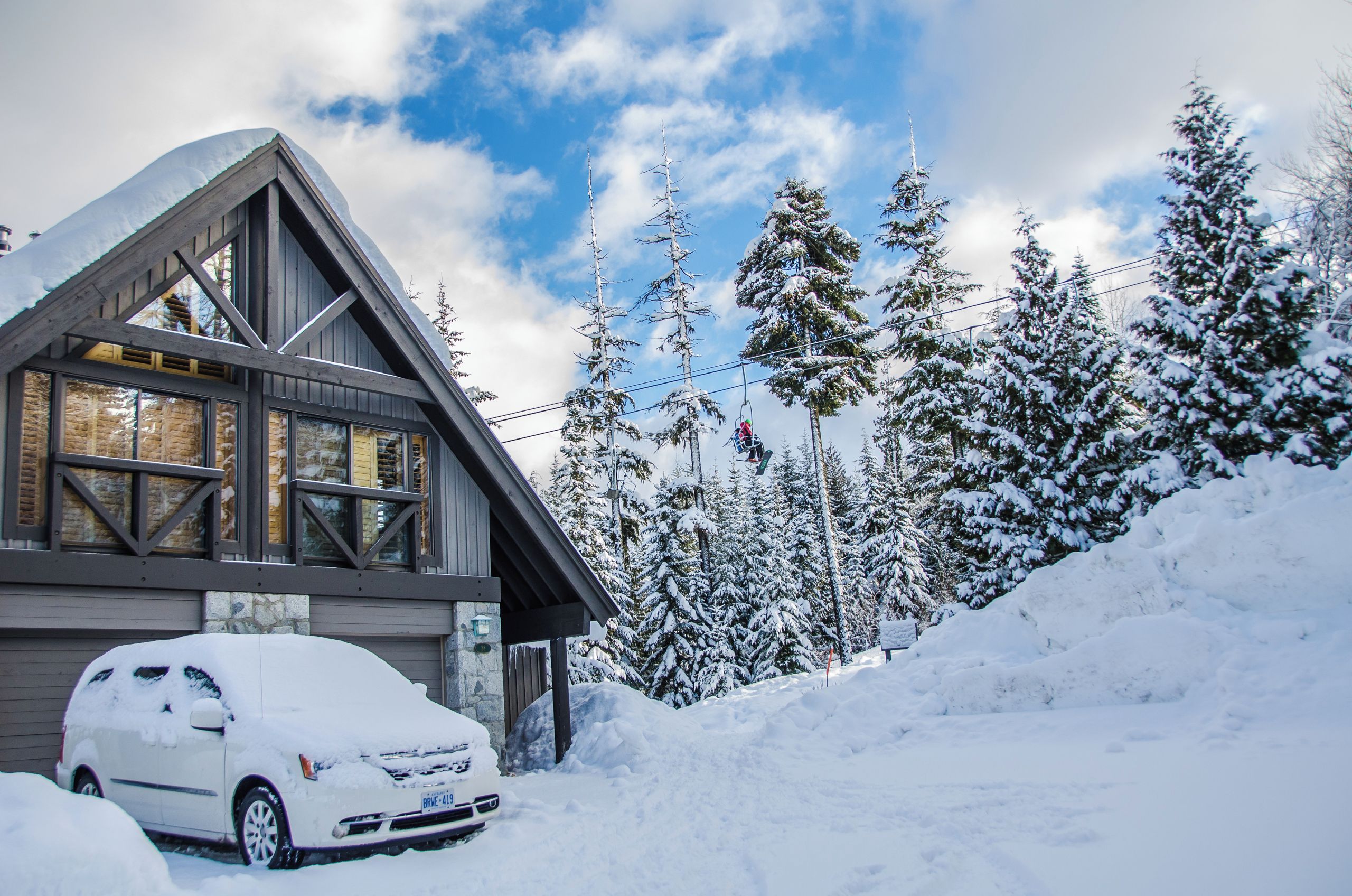 A cabin with a sloped roof, large windows, and a car parked in front.