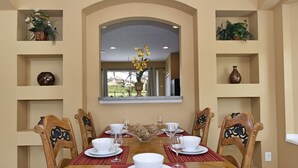 Un coin repas avec une table en bois dressée pour six personnes, entourée de chaises. Les murs sont décorés et une fenêtre se trouve au-dessus de la table.