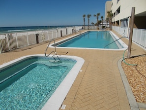 Two rectangular swimming pools with clear blue water, surrounded by a white fence and a brick walkway.