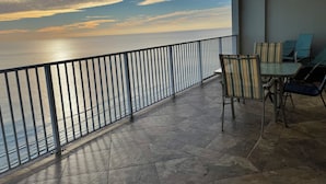 Un balcon avec vue sur la mer, un sol carrelé et une table avec des chaises.