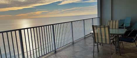 Un balcón con vistas al mar, piso de baldosas y una mesa con sillas.