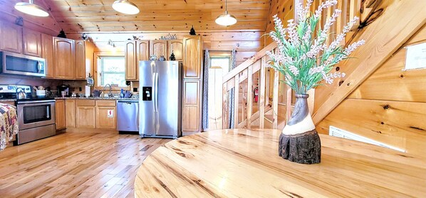A kitchen with wooden cabinets, stainless steel appliances, and a wooden dining table with a vase of flowers.