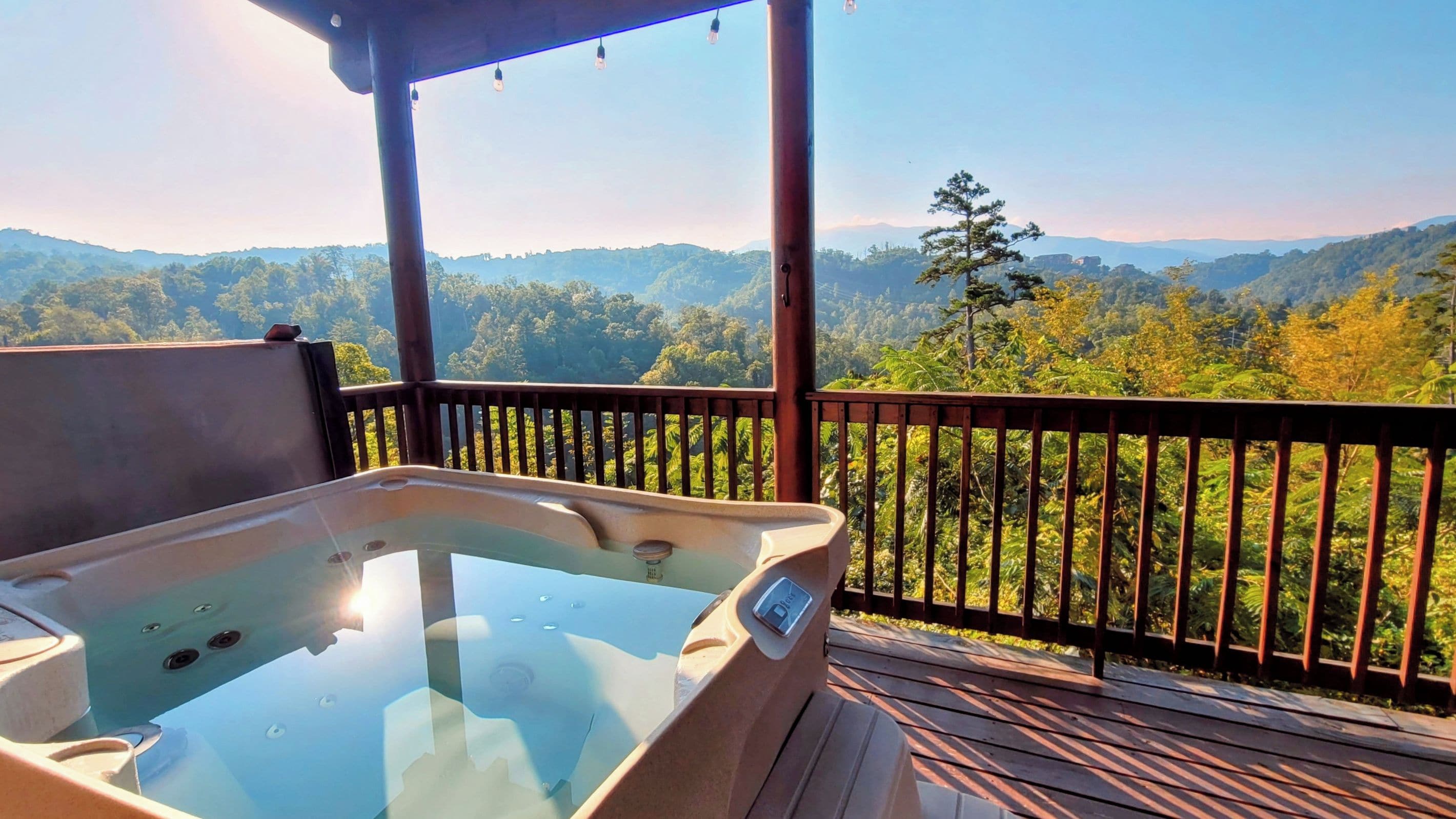 Een hottub op een houten terras met uitzicht op een bebost berglandschap.