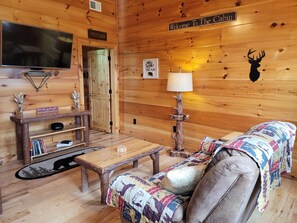 A cozy cabin interior with a wooden interior, a television, a fireplace, and a sign reading "Welcome to the Cabin".