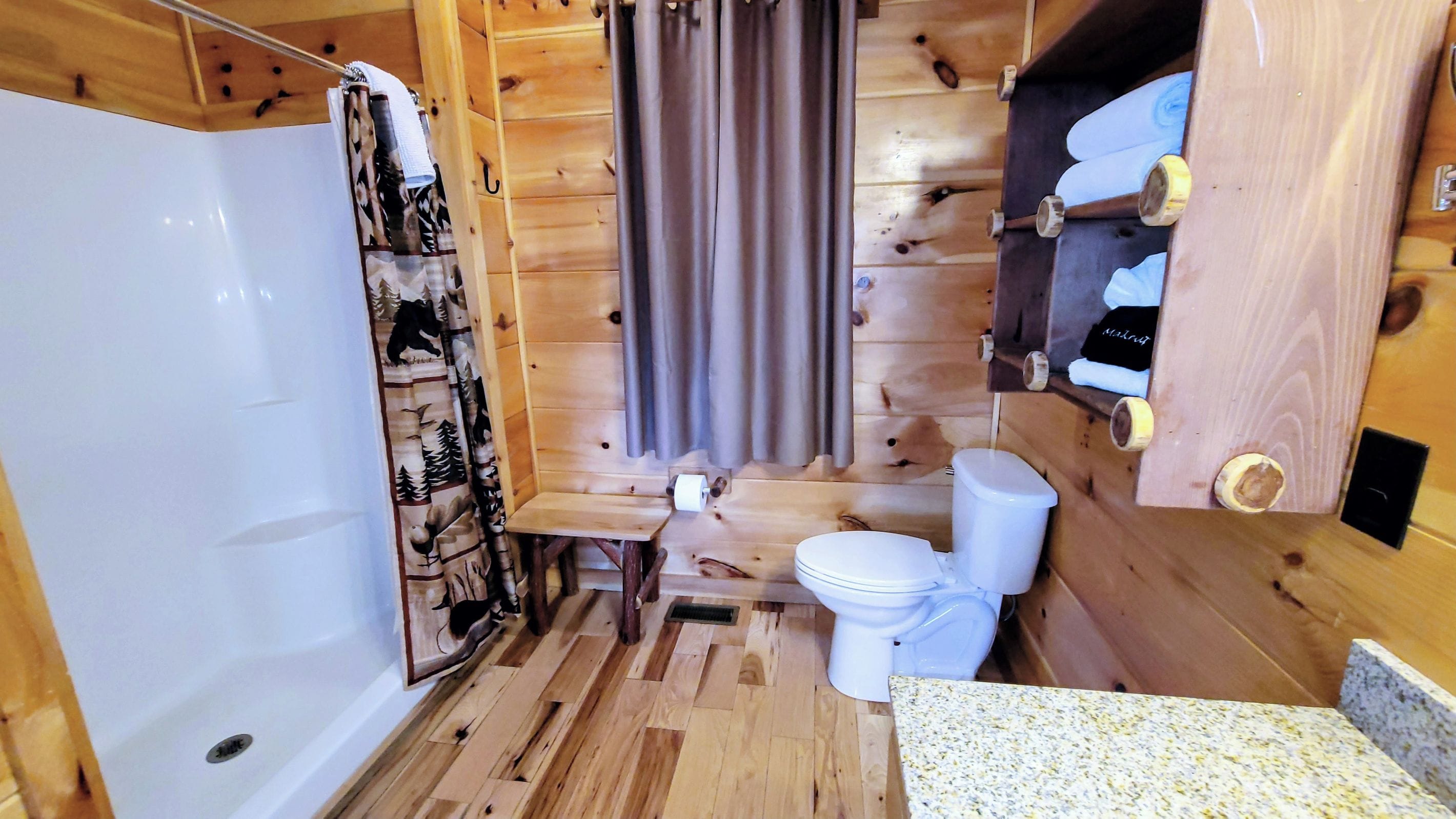 A wooden cabin bathroom with a shower, toilet, and a small vanity area.