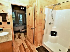 Une salle de bain en bois équipée d’une douche, d’un lavabo et d’une porte donnant sur une chambre.