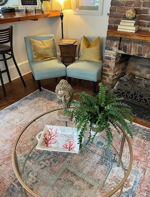 A cozy living room with two light blue armchairs, a round coffee table with a decorative item, a small side table, and a brick fireplace.