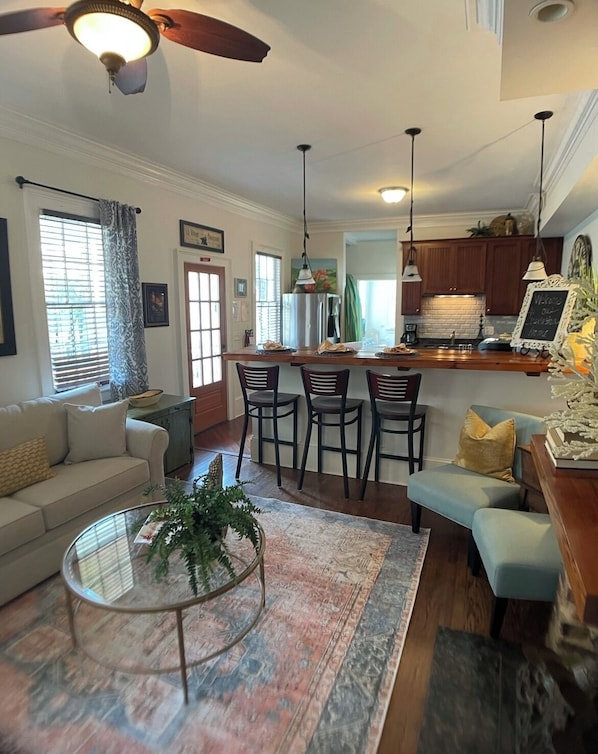 A modern living room with a sofa, a coffee table with a plant, and a dining area with chairs and a kitchen in the background.
