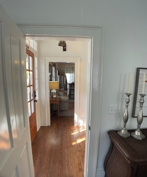 A hallway with wooden flooring leading to a kitchen area with a refrigerator and a dining table.