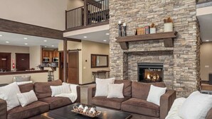 A spacious living room with a stone fireplace, a kitchen in the background, and a balcony. - The Leavenworth Lodge - Swimming Pool, Pickleball (Leavenworth)