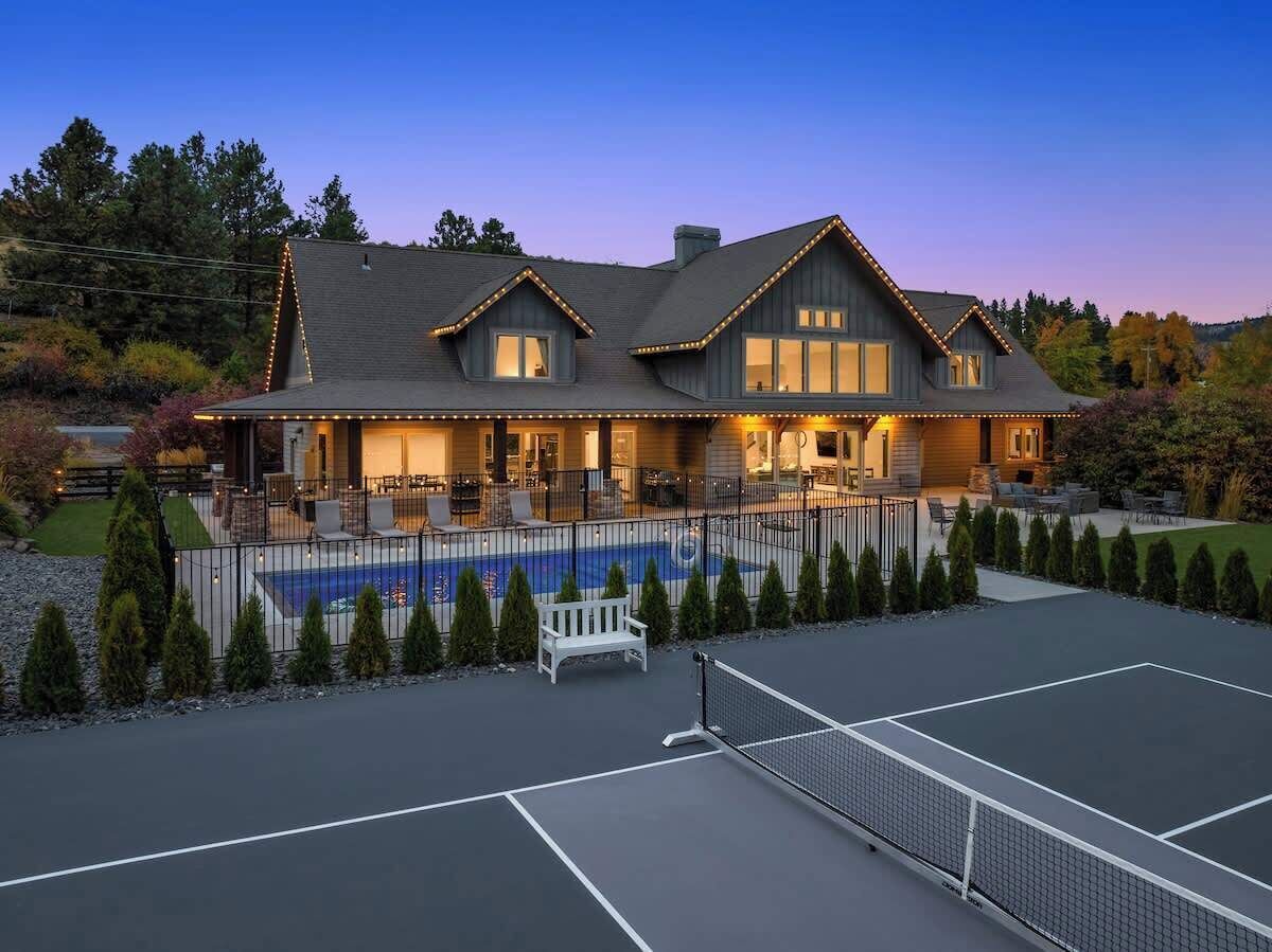 A large house with a swimming pool, tennis court, and a well-lit outdoor area.
