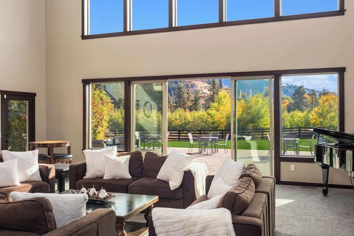 A spacious living room with a sectional sofa, a piano, and large windows offering a view of a landscaped garden.