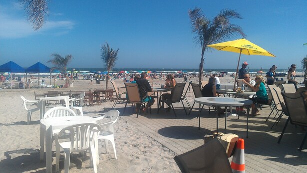 Ein Restaurant direkt am Strand mit Außenbereich, Tischen und Stühlen mit Blick auf Strand und Meer.