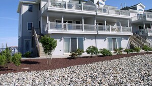 Ein mehrstöckiges Anwesen am Strand mit Balkonen, einer Treppe und einem angelegten Garten.