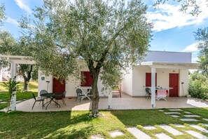 A patio area with outdoor seating, a tree, and a building with red doors. - Villaggio Turistico Baia Del Monaco (Monte Sant'Angelo)