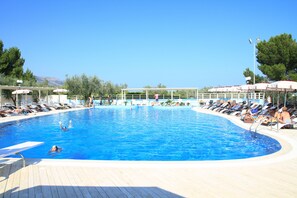 A large outdoor swimming pool with sun loungers and umbrellas, surrounded by trees and a clear sky. - Villaggio Turistico Baia Del Monaco (Monte Sant'Angelo)