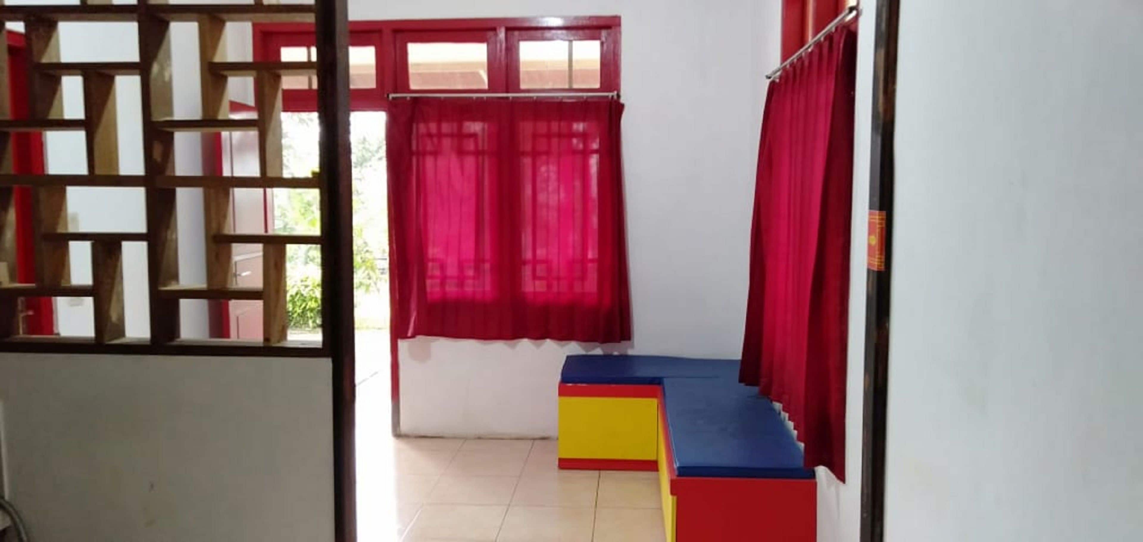 A room with a window, red curtains, a colorful bench, and a wooden partition.