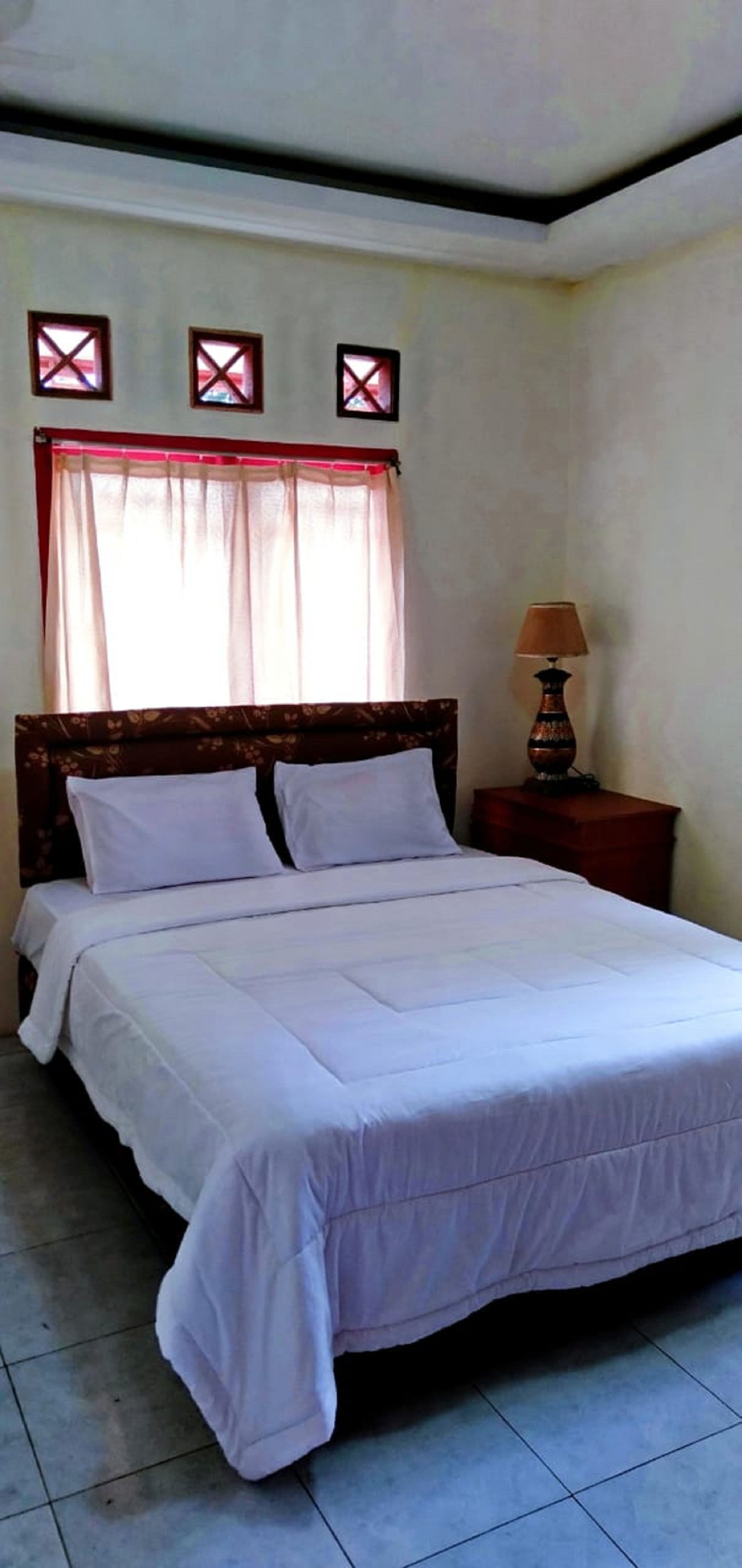 A neatly made bed with white linens in a room with a tiled floor and a wooden headboard.